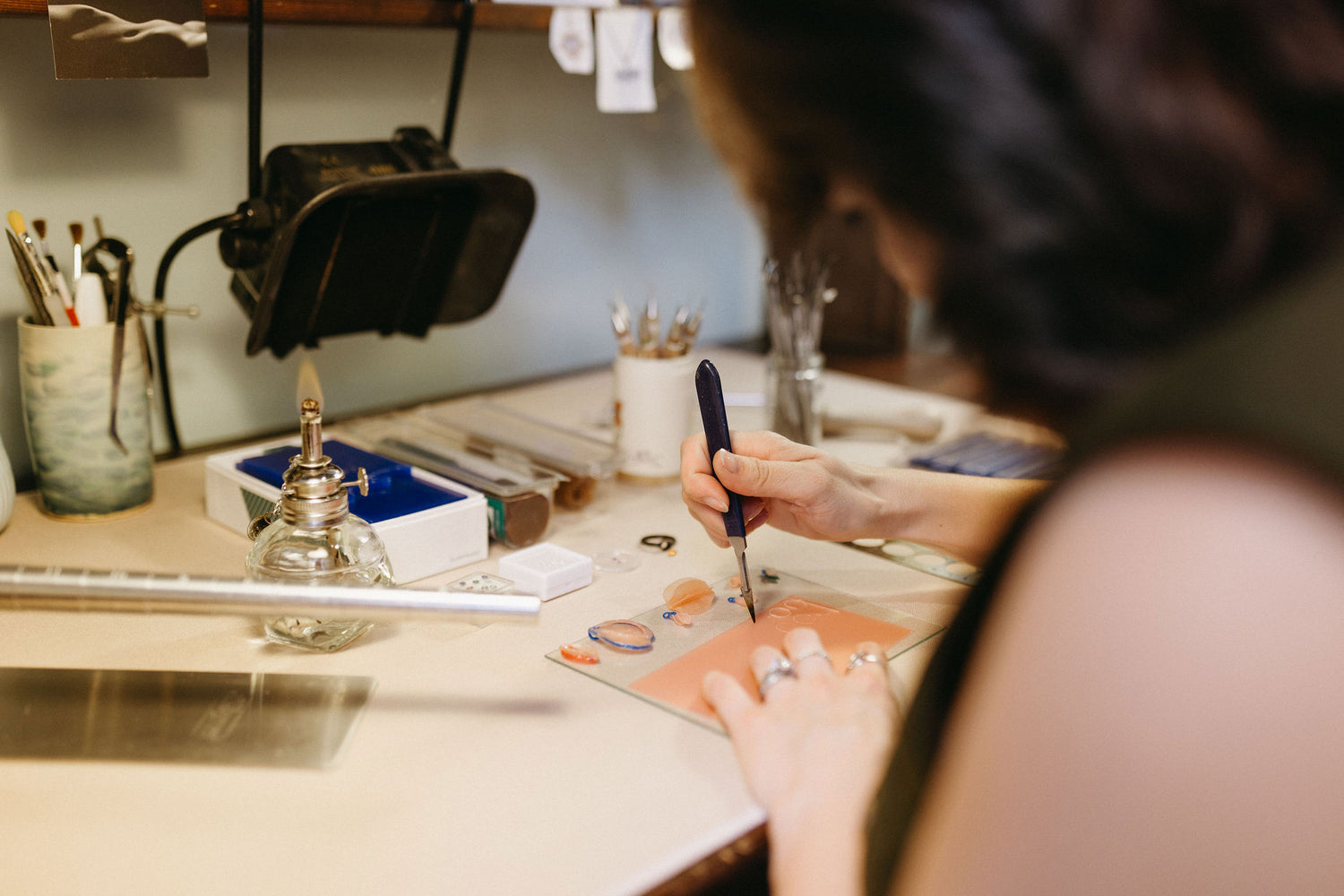 Jewelry artist working at her desk with various tools and wax molds.