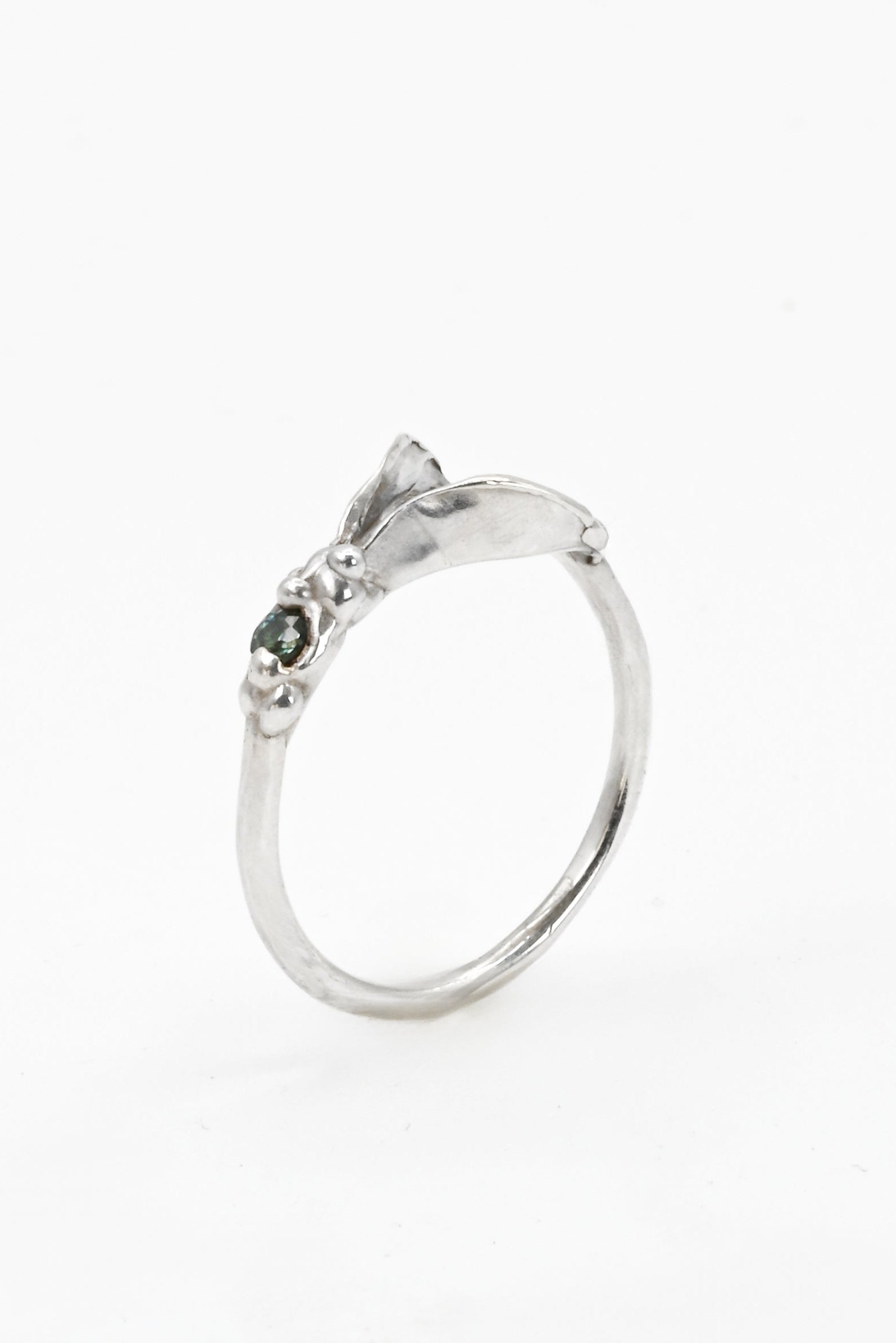 Silver impurity ring with a small teal sapphire gemstone on a white background