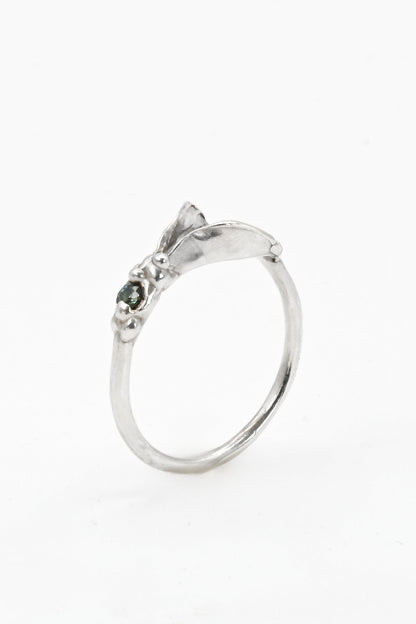 Silver impurity ring with a small teal sapphire gemstone on a white background