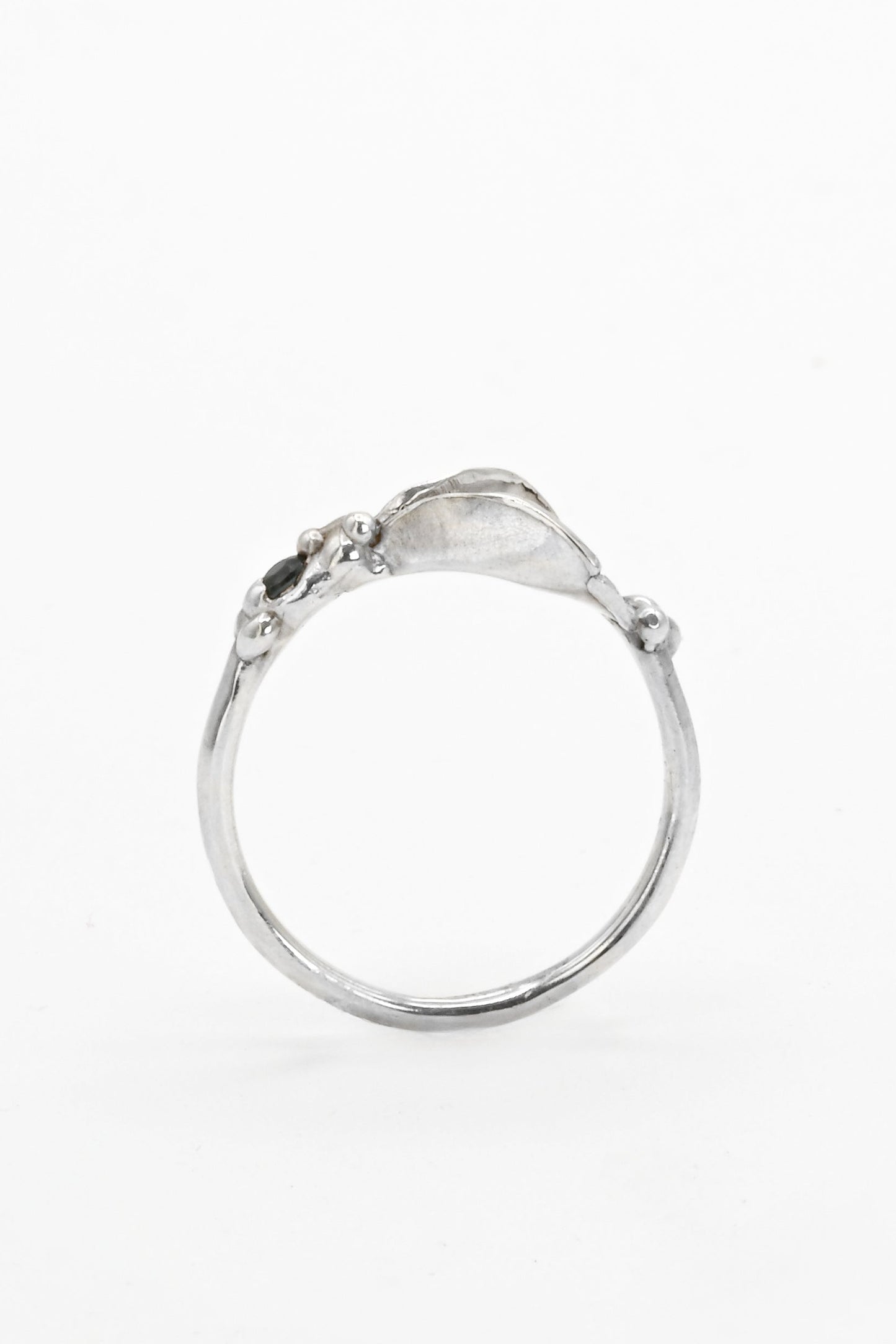Side view of a silver impurity ring with a teal blue sapphire gemstone and vulva design by Impurity Culture