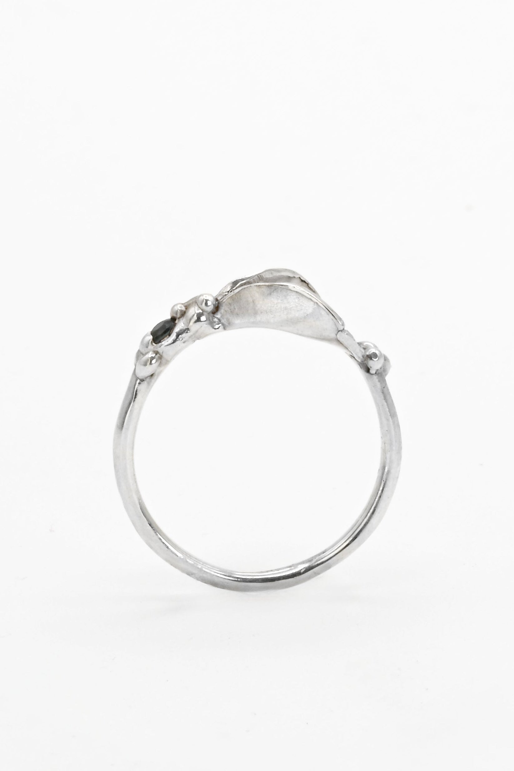 Side view of a silver impurity ring with a teal blue sapphire gemstone and vulva design by Impurity Culture