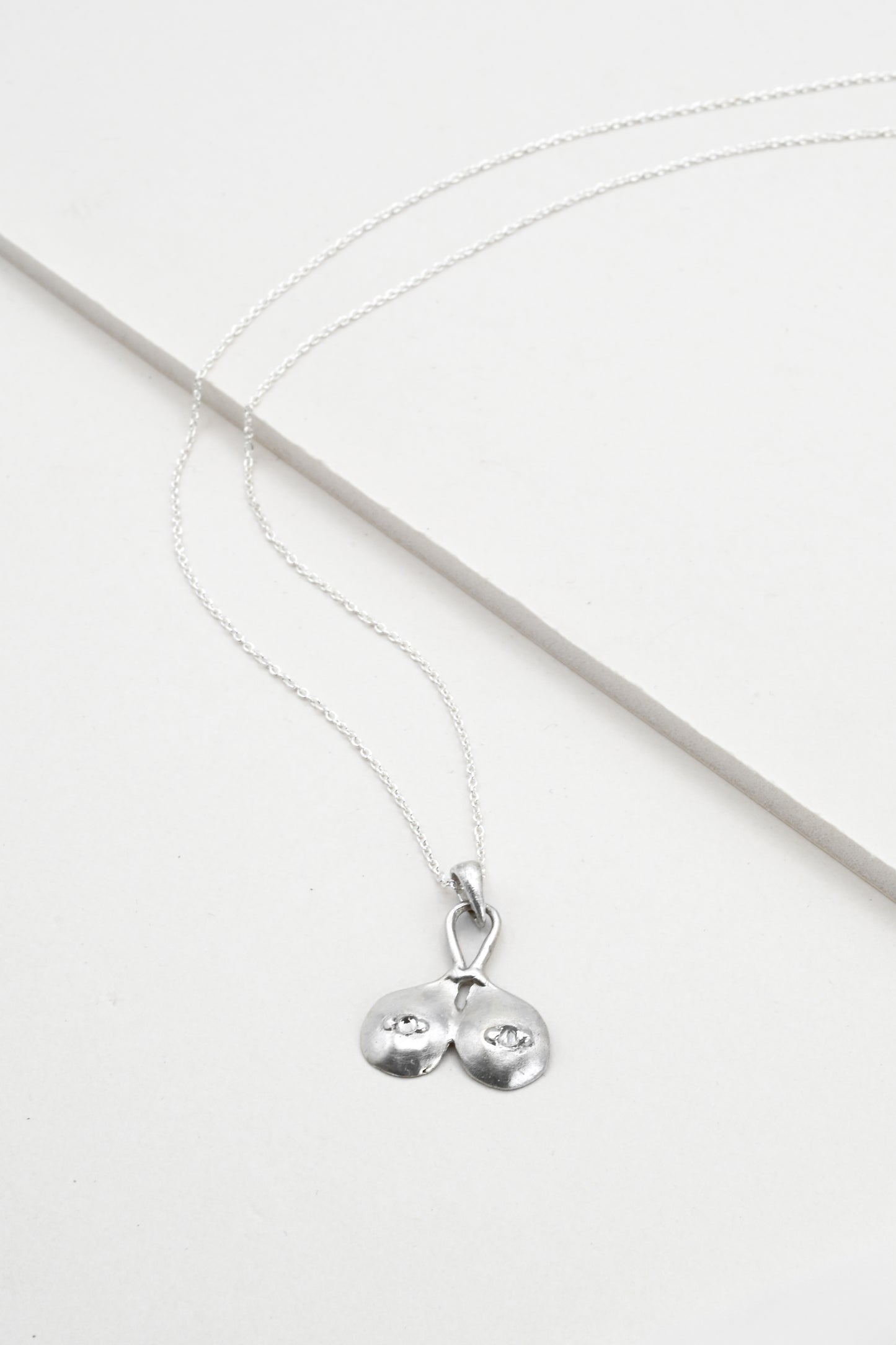 Flat lay view of "Godiva" silver breasts pendant with white sapphire nipples, by Impurity Culture Jewelry