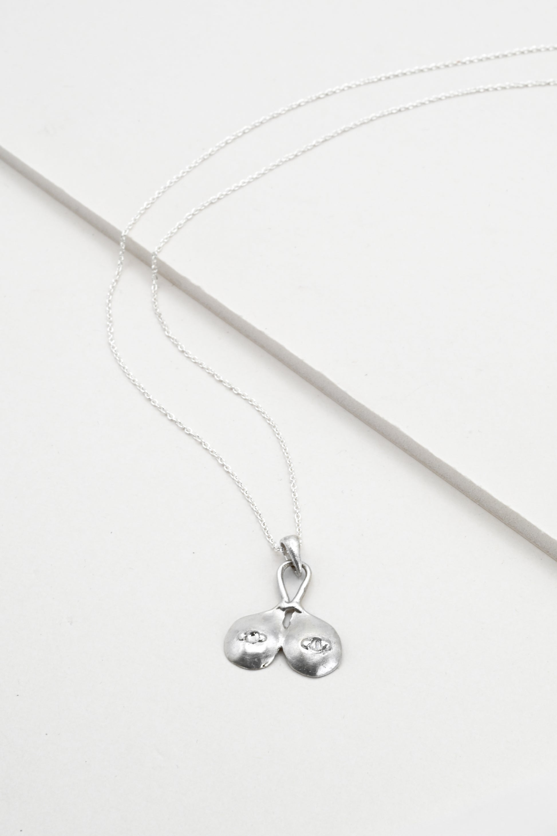 Flat lay view of "Godiva" silver breasts pendant with white sapphire nipples, by Impurity Culture Jewelry