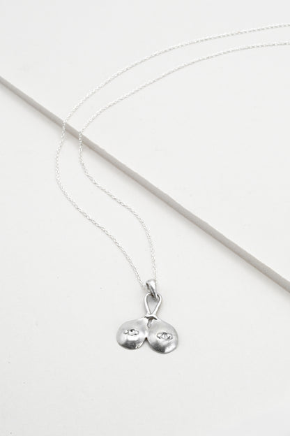 Flat lay view of "Godiva" silver breasts pendant with white sapphire nipples, by Impurity Culture Jewelry