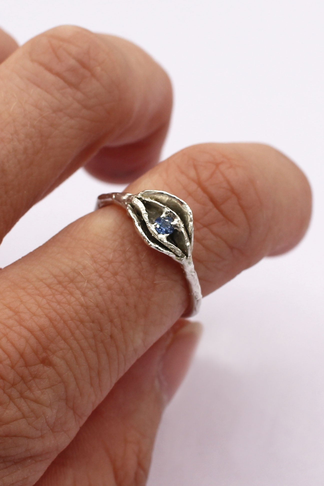 Modeled photo of a sterling silver cast vulva "impurity ring" with layered petal focal and small periwinkle sapphire center. Yoni ring made by Alison Jefferies for Impurity Culture Jewelry.
