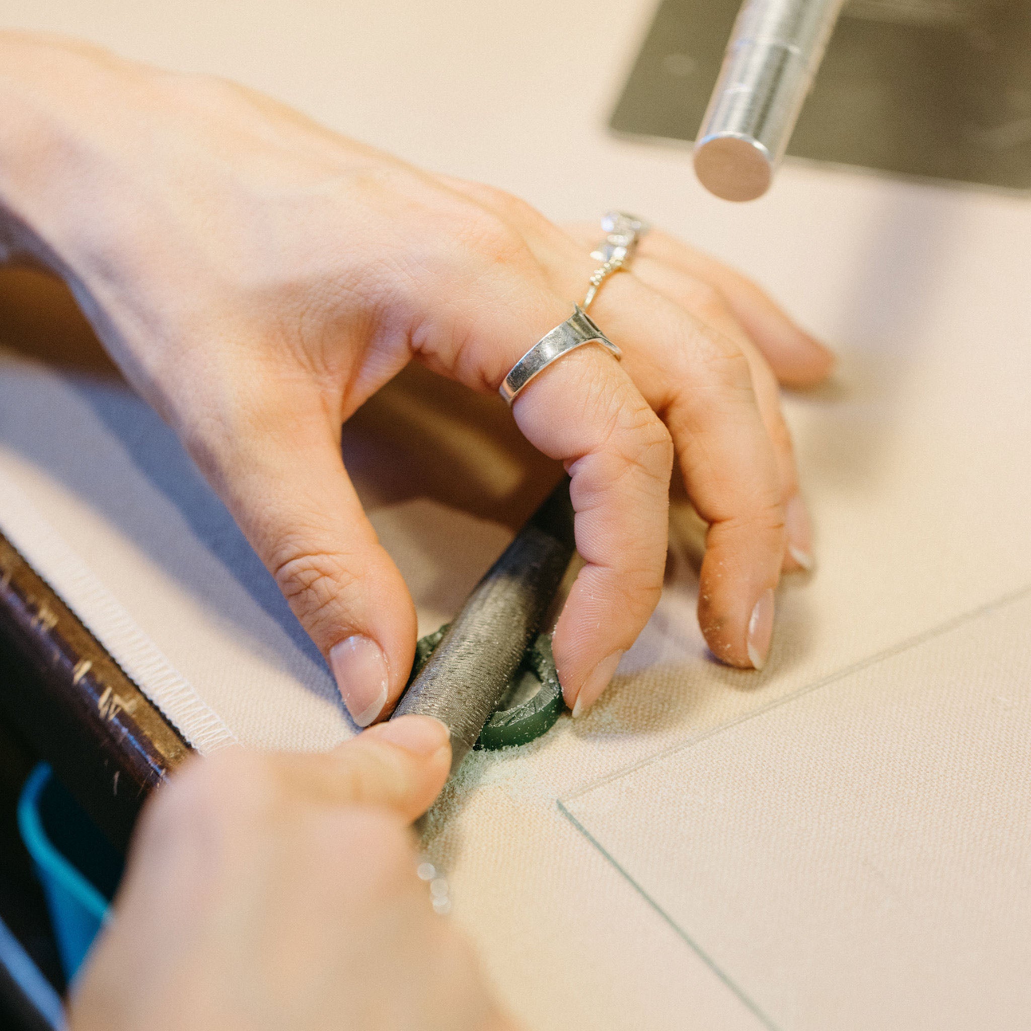 Close-up of a jewelry artist's hands shaping a green wax mold with a metal file, focusing on the detailed work in the jewelry-making process.