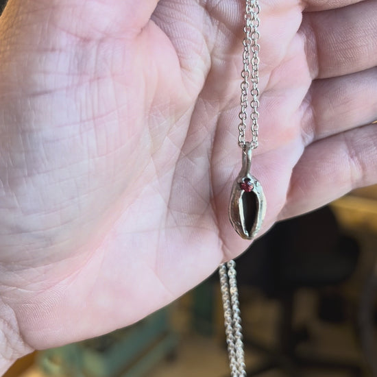 Sterling silver yoni necklace with a red sapphire, held in the hand of a white woman. Feminist jewelry by Impurity Culture.