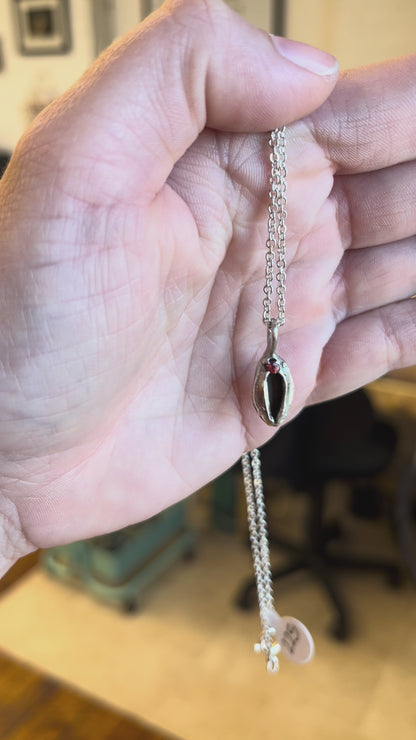Sterling silver yoni necklace with a red sapphire, held in the hand of a white woman. Feminist jewelry by Impurity Culture.